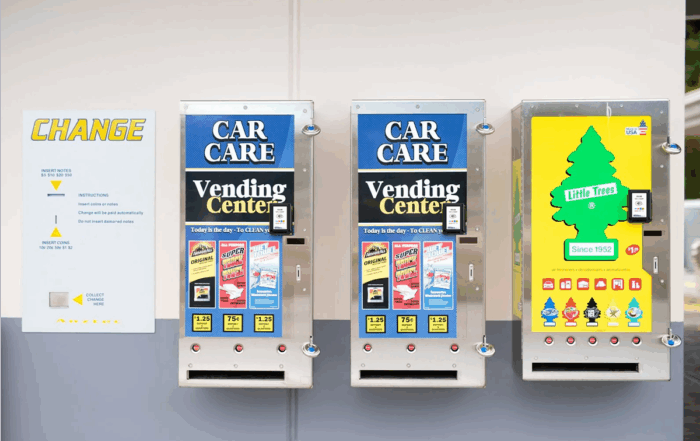 Wall-mounted car care vending machines with digital payment terminals offering cleaning products and air fresheners at a car wash.