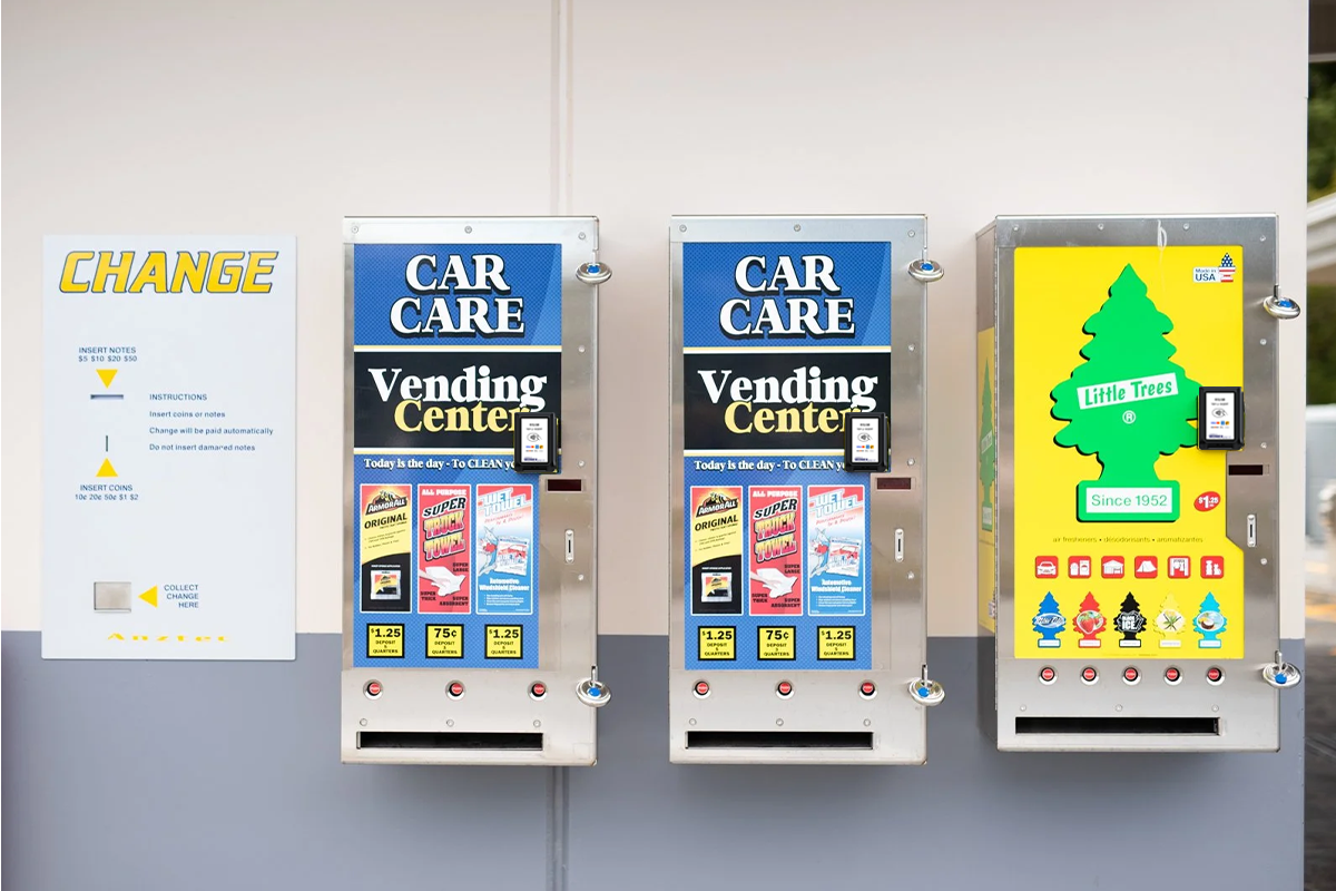 Wall-mounted car care vending machines with digital payment terminals offering cleaning products and air fresheners at a car wash.