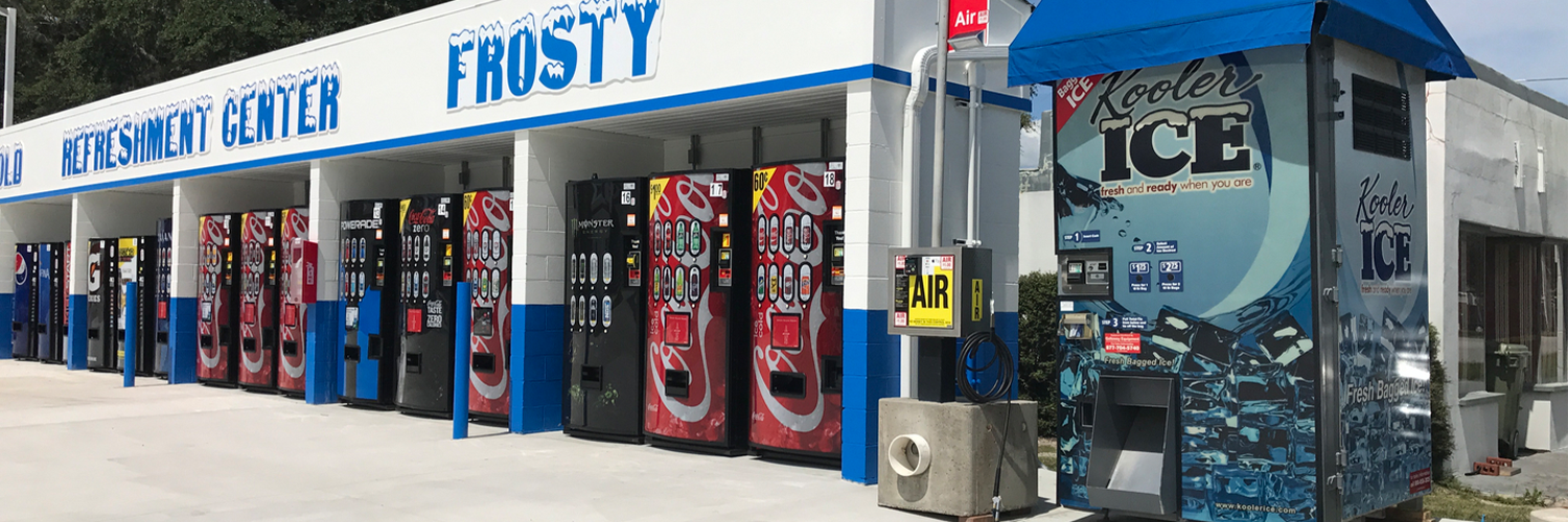 Row of beverage vending machines and an ice vending station outside a car wash refreshment center offering cold drinks and bagged ice.